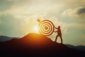 Silhouette of businessman pushing a target board on top of the hill. Concept of aim and objective...