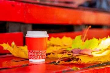 Small cardboard blank takeaway coffee cup on bench in autumn. Fallen leaves. Close-up. Warm up with aromatic coffee.Hot drink.season, advertisement and drinks concept, mock up