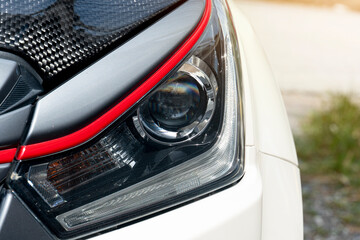 Abstract of luxury or used of headlights of car. Car in the parking lot with blurred of green grass outside at day.