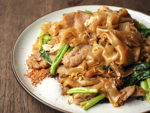 dish of PAD SEE EW, Thai stir-fried flat noodles, Chinese kale and pork meat, egg with dark sweet soy sauce, served with chili flakes and sugar