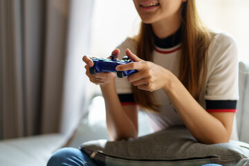 Lovely Asian woman sitting on sofa and relaxing playing games wearing VR glasses while playing games at her home with lots of fun and enjoyment.