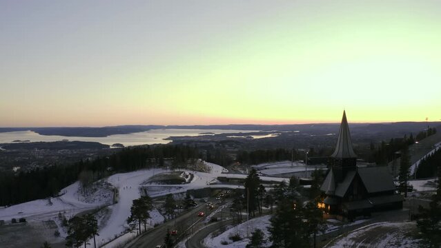 Oslo city drone wrap around Holmenkollen chapel church, with Holmenkollbakken ski jump, Oslo Vinterpark Winterpark Tryvann at Sunset 