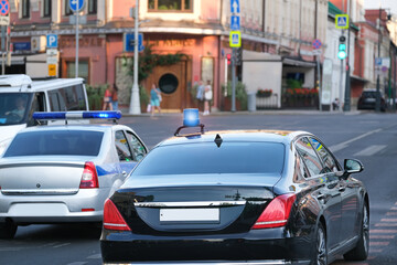 Fototapeta na wymiar Police car with flasher and luxury car with flasher on city street