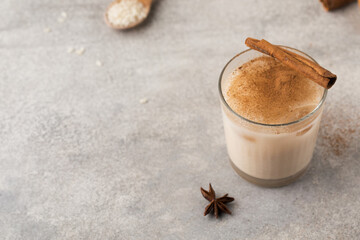 Homemade Horchata rice drink in a glass with ice and cinnamon stick on a gray concrete background....