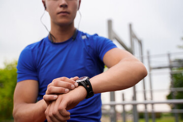 Shot of blond haired athlete dressed in sportswear setting timer on his watch outdoors in city.