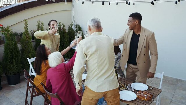 Family and friends celebrating at dinner on a rooftop terrace. Multiethnic group of people dining on the balcony on a special evening to celebrate friendship and family love and relationships
