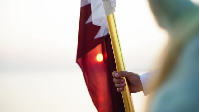 A knight holding Qatar flag on horse near the sea in Qatar desert