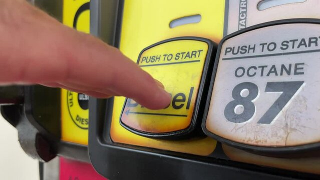 Caucasian hand selects diesel at fuel pump at gas station; close up