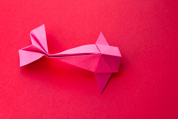 Pink paper fish origami isolated on a red background