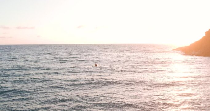 Determined man on kayak paddling against the waves in golden sunrise, drone view
