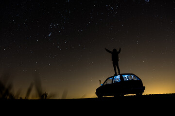 A man standing on a car in the background of stars with a night sky, a shining galaxy