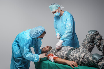 Shot of surgeon specialist and his assistant bandaging wounded military man.