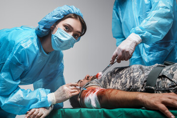Shot of surgeon specialist and his assistant bandaging wounded military man.