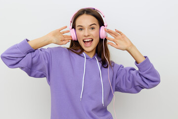 horizontal studio photo of a happy, joyful woman in a purple tracksuit listening to music holding her pink headphones with both hands and smiling broadly looking at the camera