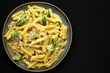 Homemade Penne Alfredo Pasta with Chicken and Broccoli on a Plate on a black background, top view. Overhead, flat lay, from above. Copy space.