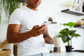 Partial view of african american man using cellphone and holding cup of coffee in kitchen 