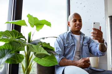 Smiling african american man holding cup and having video call on smartphone at home 