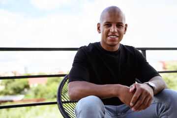 Smiling african american man looking at camera on armchair on balcony 