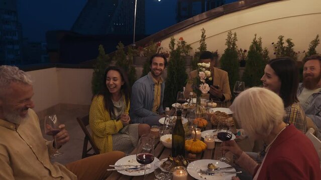 Family and friends celebrating at dinner on a rooftop terrace. Multiethnic group of people dining on the balcony on a special evening to celebrate friendship and family love and relationships