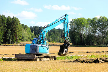Blue Compact Tracked Excavator at Work Digging a Trench in Field
