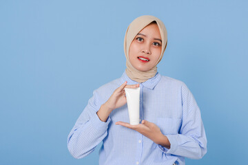 Smiling muslim beautiful woman with hijab and casual shirt standing over isolated light blue...