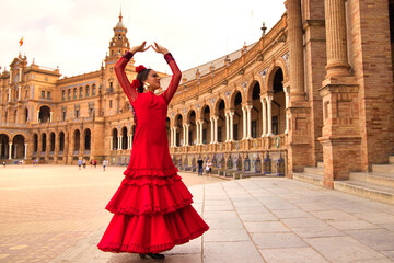 Beautiful teenage woman dancing flamenco in a square in Seville, Spain. She wears a red dress with ruffles and dances flamenco with a lot of art. Flamenco cultural heritage of humanity. - obrazy, fototapety, plakaty
