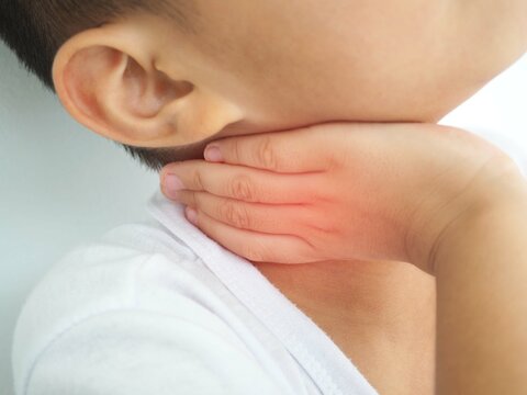 Sick Asian Kid Touching His Painful Neck, Sore Throat And Flu, Throat Infection On White Background. Closeup Photo, Blurred.