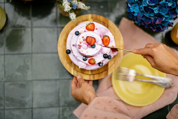 Female cuts berry cheese cake on table decorated with flowers, view from above, Sweet holiday...