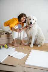 Young woman makes selfie photo on phone with her cute dog, have fun while making repairing at new apartment. Happy improvement and house repairing concept