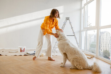 Young woman plays with her dog in room while making repairing in apartment. Fun during house...