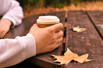Fototapeta na wymiar Paper glass of coffee in hand on the orange autumn leaves background