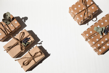 A set of handmade gifts in kraft paper, tied with wide twine, decorated with dry flowers on a white table. Top view