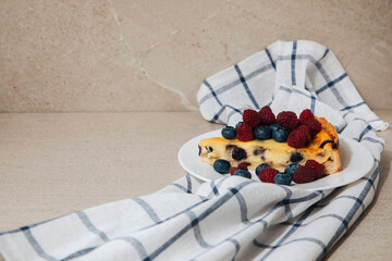 A piece of blueberry cheesecake on a white plate with raspberry on a white towel in a cage. Front view
