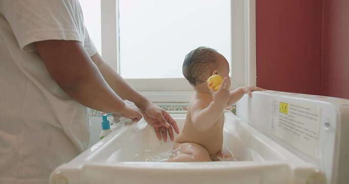 happy little cute Asian baby joy bathing in bathtub and play water having fun smiling at bathroom home, father care hygiene clean wash water body baby care, childhood healthcare hygiene baby care 