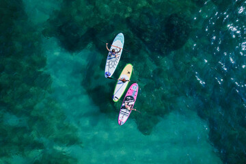 Aerial drone view of three paddle surfers over crystalline waters. High-quality 4k footage