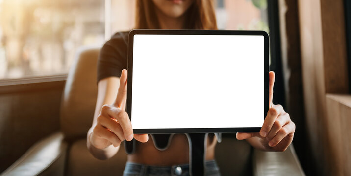 Mockup image of a beautiful woman holding and showing a tablet and smartphone with blank white screen while sitting at cafe.