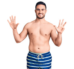 Young handsome man wearing swimwear showing and pointing up with fingers number nine while smiling confident and happy.