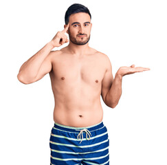 Fototapeta premium Young handsome man wearing swimwear confused and annoyed with open palm showing copy space and pointing finger to forehead. think about it.