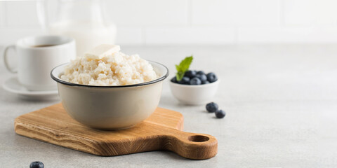 Rice porridge or pudding with a piece of butter, a mug of coffee and blueberries in a bowl. Copy space