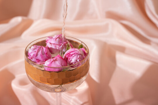 Champagne with flowers in glass on folded fabric background. Creative holiday concept