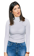 Beautiful brunette woman wearing casual clothes in shock face, looking skeptical and sarcastic, surprised with open mouth