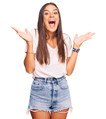 Young hispanic woman wearing casual white tshirt celebrating crazy and amazed for success with arms...