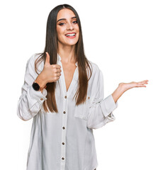 Young beautiful woman wearing casual white shirt showing palm hand and doing ok gesture with thumbs up, smiling happy and cheerful