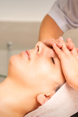 Fototapeta premium Facial massage. Young caucasian woman with closed eyes getting a massage on her forehead in a beauty salon