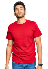 Young handsome man wearing casual red tshirt looking at the camera blowing a kiss on air being lovely and sexy. love expression.