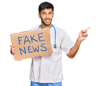 Young handsome man wearing doctor uniform holding fake news banner smiling happy pointing with hand and finger to the side