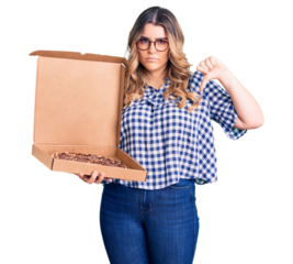 Young caucasian woman holding delivery pizza box with angry face, negative sign showing dislike with thumbs down, rejection concept