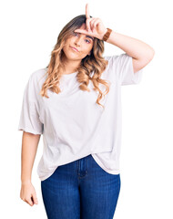 Fototapeta premium Young caucasian woman wearing casual clothes making fun of people with fingers on forehead doing loser gesture mocking and insulting.