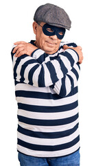 Senior handsome man wearing burglar mask and t-shirt hugging oneself happy and positive, smiling...