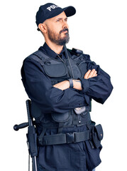 Young handsome man wearing police uniform looking to the side with arms crossed convinced and confident